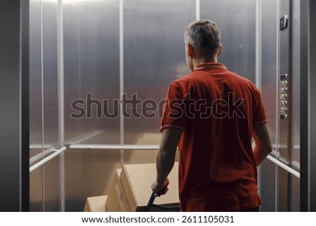 Delivery man getting in the elevator and pushing a hand truck loaded with boxes, back view