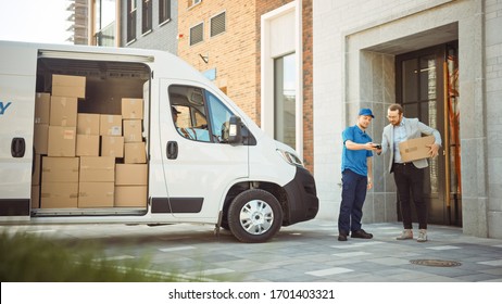 Delivery Man Gives Postal Package To A Business Customer, Who Signs Electronic Signature POD Device. In Stylish Modern Urban Office Area Courier Delivers Cardboard Box Parcel To A Man.