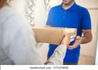 Delivery Man Handing Box To Woman. Woman Receiving Package From A Delivery Man. Woman Wearing Shirt Receiving Package From Courier At The Office. 