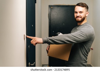 Delivery Man Holding Cardboard Box And Contactless Payment POS Wireless Terminal For Card Paying And Ringing Doorbell Of Customer Apartment, Looking At Camera. Concept Of Online Shopping.