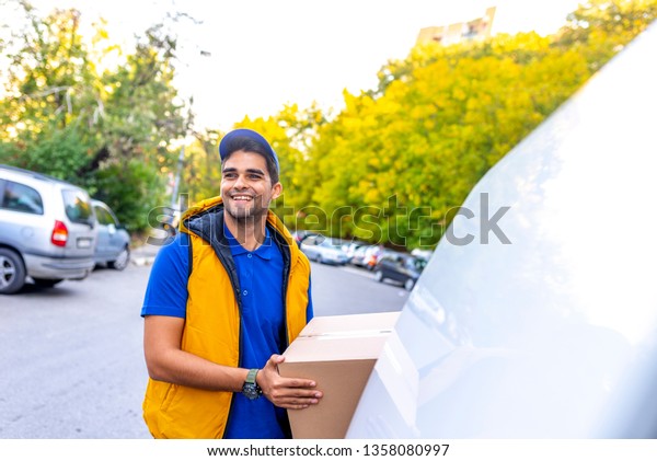 Delivery man\
holding cardboard boxes / copy space. Portrait of an handsome happy\
deliverer with box. Smiling delivery man in red uniform giving a\
box - courier service concept\
