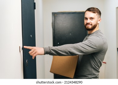 Delivery man holding in hand cardboard box with parcel and ringing doorbell of customer apartment, looking at camera. Side view of courier male delivering online order rings doorbell in doorstep.