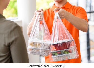 Delivery Man In Orange Uniform Delivering Asian Food Boxes In Plastic Bags To A Woman Customer At Home