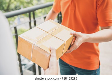 Delivery man in orange uniform handing a parcel box over to a customer  - courier service concept