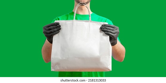 Delivery Man With Paper Bag. Courier In Uniform T-shirt, Gloves Service Fast Delivering Orders. Young Guy Holding A Paper Package. Character On Isolated Background For Mockup Design.