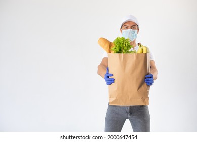 A Delivery Man In A Protective Mask And Gloves Holds A Craft Bag With Groceries.