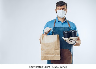 Delivery Man In Protective Mask And Medical Gloves Holding Takeaway Food. Compliance With The Hygiene Rules While Covid-19 Pandemic. Safe Service