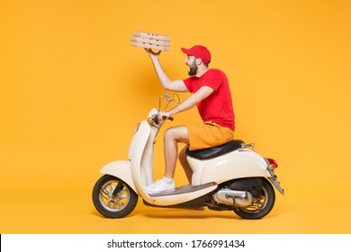 Delivery man in red cap t-shirt uniform driving moped motorbike scooter hold pizza in cardboard flatbox isolated on yellow background studio Guy employee working courier Service quarantine concept