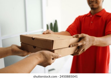 Delivery man in red uniform deliver two boxes of pizza to customer. Fast food delivery concept. - Powered by Shutterstock