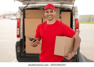 Delivery man with tablet and box standing near van, smiling at camera. Logistics and courier concept