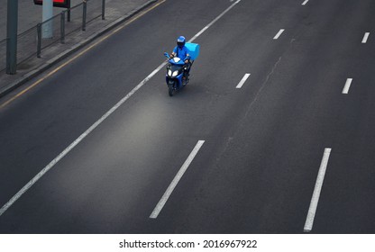 Delivery Man Of Takeaway Food Service On Scooter With Trunk Case Box Driving Fast. Courier Delivering Food By Scooter. Pizza Delivery Boy Riding Motor Bike On The City Street In Evening, Take Out Food