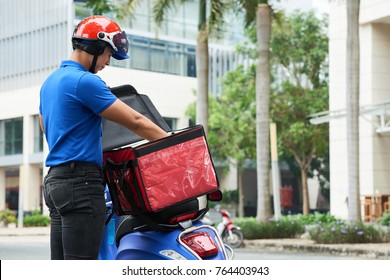 Delivery Man Taking Food Out Of Bag On His Scooter