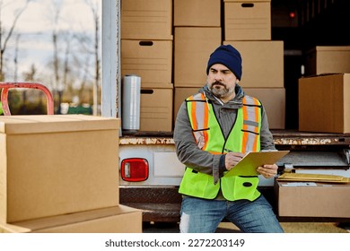 Delivery man taking notes while checking packages before the shipment at back of the truck.