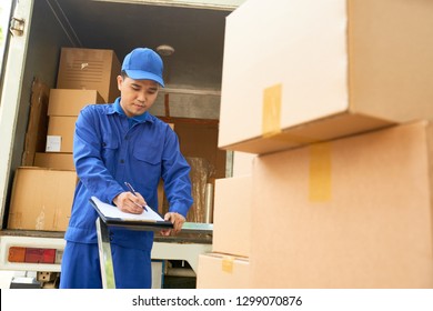 Delivery Man In Uniform Loading Truck And Taking Notes In Document