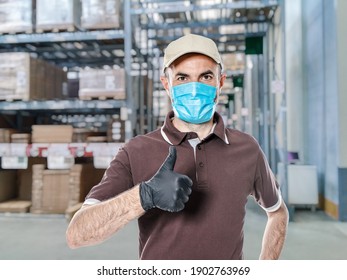 Delivery Man With Uniform And Protective Mask For Covid-19 Inside A Warehouse. Safe Shipping Concept.