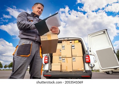 Delivery man at work. Courier van in background. Cardboard boxes inside courier van. Delivery service worker. Career in courier company. Male postman writes something. Provision of delivery services - Shutterstock ID 2053541069