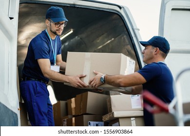 Delivery men loading carboard boxes in a van while getting ready for the shipment. 