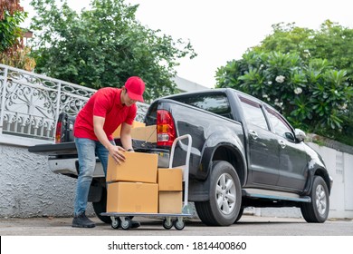 Delivery men in red uniform unloading cardboard boxes from pickup truck. Courier man sending the parcel or package to the customer on a business day. Online shopping and transport logistics concept.