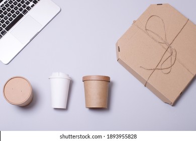 Delivery, Online Ordering Food To The Office, Busy Day, Eco-friendly Packaging, Fast Food Concept. Several Types Of Food Containers, Cardboard Box For Pizza, Laptop On A Gray Background. Flat Lay.