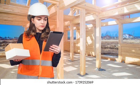 Delivery Of Order. Courier Service. Delivery Of Construction Materials. A Girl With A Tablet And Boxes On The Background Of The Frame Of The House.