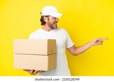 Delivery senior dutch man isolated on yellow background pointing finger to the side and presenting a product