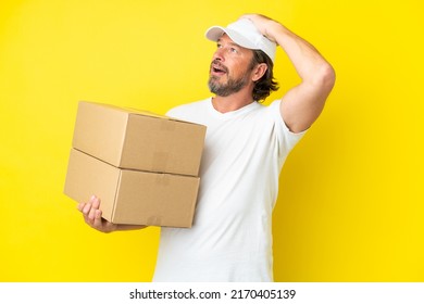 Delivery senior dutch man isolated on yellow background doing surprise gesture while looking to the side