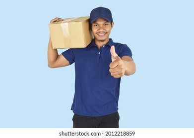 Delivery service concept.  Delivery man holding box and showing like on blue background. happy man with parcel boxes showing thumbs up.