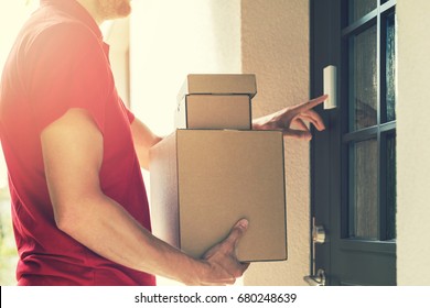 delivery service courier ringing the house doorbell with boxes in hands