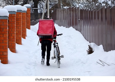 Delivery Service Courier With A Thermos Bag With Bicycle Walking Down The Snow In Winter City. Food Delivery Home