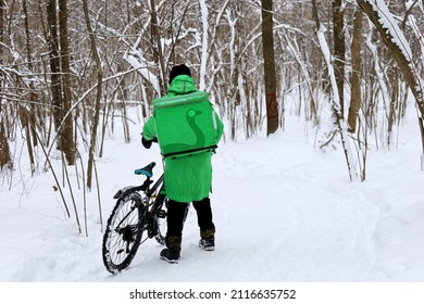 Delivery Service Courier With A Thermos Bag And Bicycle By The Snow In A Park. Food Delivery Home In Winter