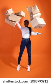 Delivery, Service, Emotions, Shipping And People Concept - Funny African-American Courier Woman In A White Cap And Rubber Gloves Catching Lots Of Boxes And Bags On Orange Background With Copy Space