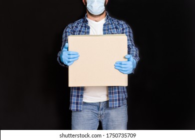 A delivery service worker in a medical face mask carrying a cardboard box in the courier's hand in protective masks and gloves hold the parcel box. - Shutterstock ID 1750735709