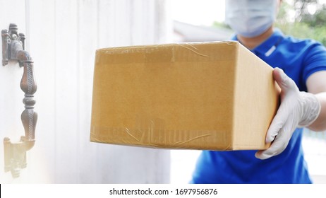 Delivery services courier during the Coronavirus (COVID-19) pandemic, close-up of cardboard box holding by a courier wearing protective face mask and latex gloves at home front door blurred background