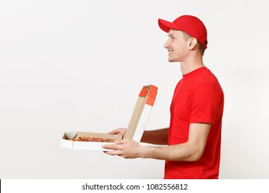 Delivery smiling man in red uniform isolated on white background. Male pizzaman in cap, t-shirt working as courier or dealer holding italian pizza in open cardboard flatbox. Copy space. Side view