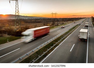 Delivery trucks and cars in high speed driving on a highway through rural landscape. Fast blurred motion drive on the freeway. Freight scene on the motorway