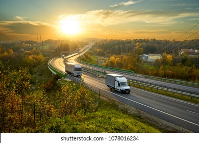 Delivery van and truck driving on the highway winding through forested landscape in autumn colors at sunset