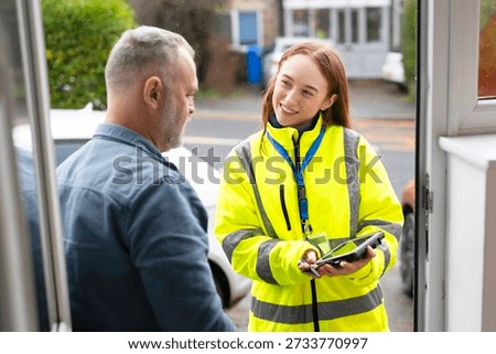 Delivery worker hands over device to customer at the front door in a suburban neighborhood