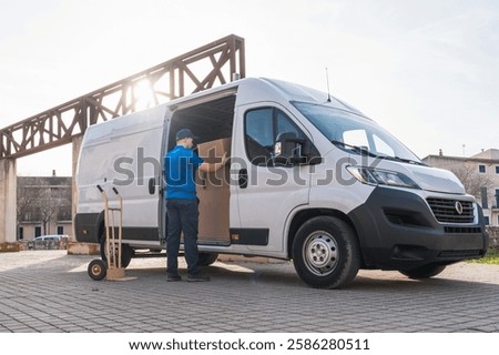 Delivery Worker Organizing Packages in Delivery Van. Delivery worker in a blue uniform arranging cardboard boxes inside an open van. Concept of logistics, distribution, and freight transportation.