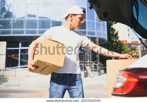 Deliveryman holds\
parcels at the car,\
delivering