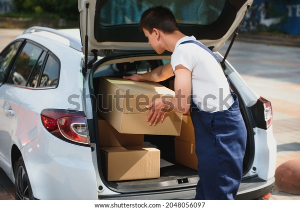 Deliveryman holds\
parcels at the car,\
delivering
