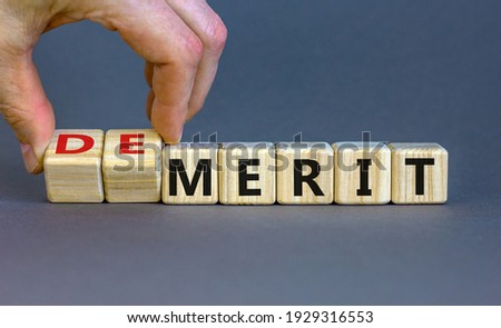 Demerit or merit symbol. Businessman turns wooden cubes and changes words 'demerit' to 'merit'. Beautiful grey background, copy space. Business and demerit or merit concept.