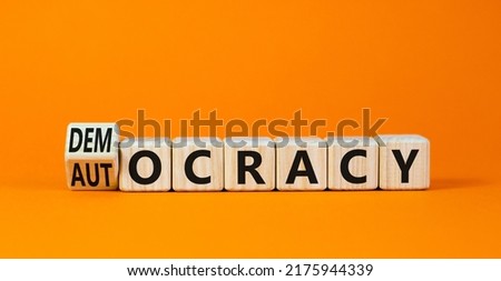Democracy or autocracy symbol. Turned wooden cubes and changed the concept word Autocracy to Democracy. Beautiful orange background. Copy space. Business democracy or autocracy concept.