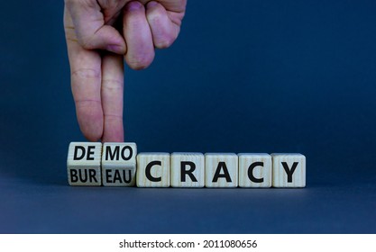 Democracy or bureaucracy symbol. Businessman turns wooden cubes and changes the word bureaucracy to democracy. Beautiful grey background, copy space. Business and democracy or bureaucracy concept.