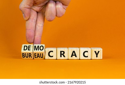 Democracy or bureaucracy symbol. Businessman turns wooden cubes and changes the word bureaucracy to democracy. Beautiful orange background, copy space. Business and democracy or bureaucracy concept.