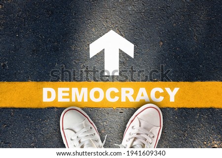 Democracy written on yellow line with white arrow on asphalt road. Future ahead concept