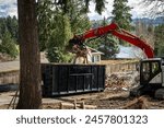 Demolition cleanup and debris removal, heavy equipment with jawbone bucket used to pickup debris and deposit in commercial dumpster for hauling away, residential construction

