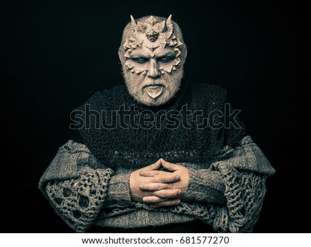 Demon with folded hands isolated on black. Alien or reptilian makeup with sharp thorns and warts. Horror and fantasy concept. Man with dragon skin and beard. Monster in grey knitted sweater.