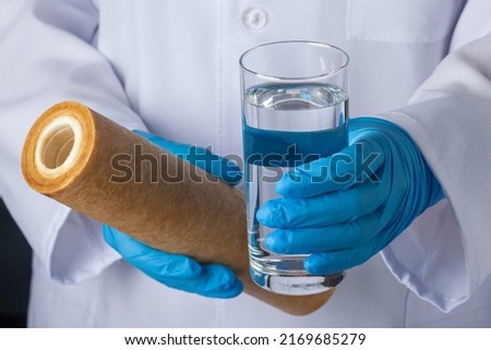 Demonstration by a laboratory assistant of a glass of purified drinking water and a used replacement filter cartridge for water treatment systems