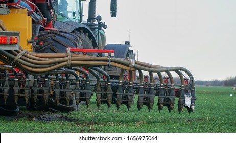 Den Ham, Netherlands - February 17, 2020 : Tractor with slurry tank and lifted injector seen from behind, busy inject manure on fields where the soil has enough bearing capacity despite wet conditions
