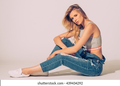 Denim beauty. Studio shot of beautiful young woman in jeans overall looking at camera while sitting on the floor